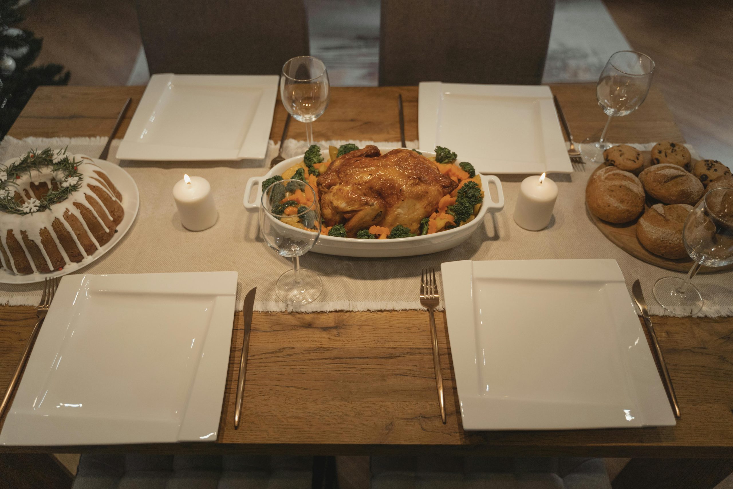 Elegant holiday dinner table setting featuring roasted chicken, cake, and bread rolls, perfect for festive gatherings.